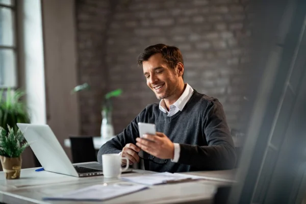 A man engaged with a laptop and cell phone at a table, showcasing a testimonial related to Linkvest Capital.